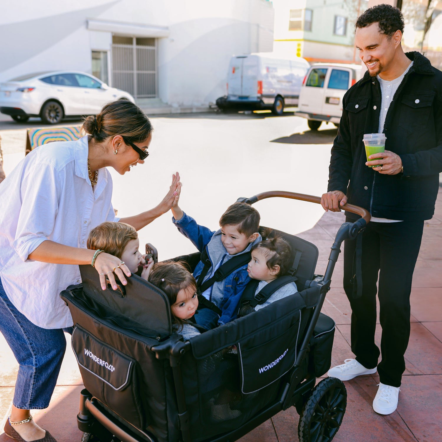 A mother high-fiving her child while they sit in the WonderFold L4 stroller wagon, with a father smiling in the background.