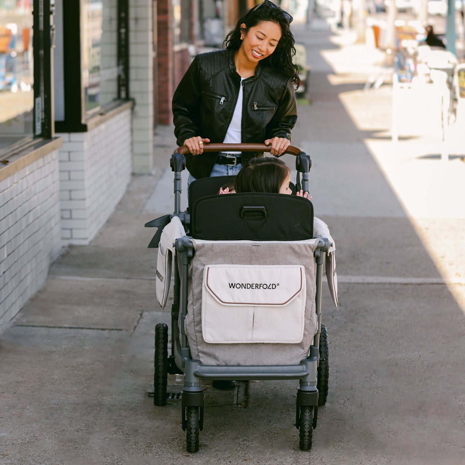 Front view of a woman pushing the WonderFold L2 stroller wagon on a city sidewalk, highlighting its spacious design